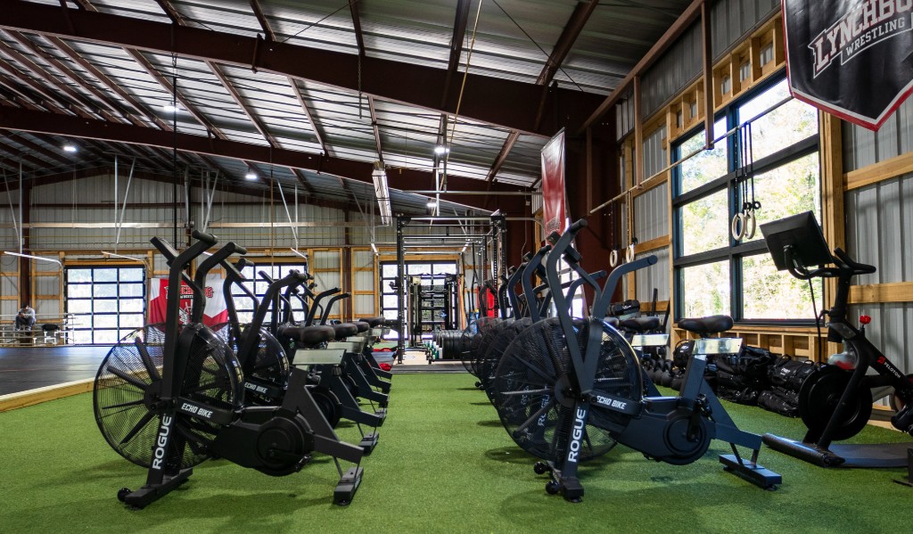Lynchburg wrestling facility strength and conditioning area: turf runway, air bikes, racks, and Lynchburg Wrestling banner