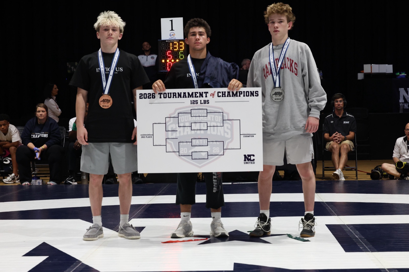 The 125 lb podium at the 2026 Tournament of Champions — the three placers on the mat, the champion holding the bracket