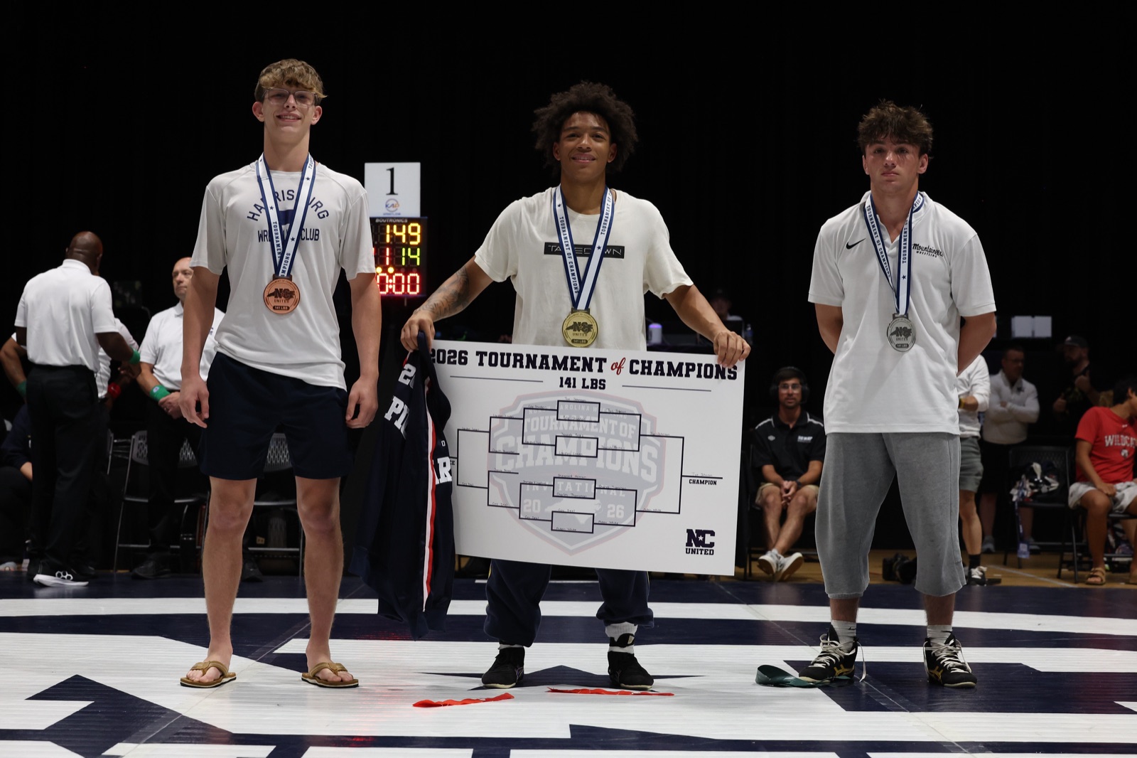 The 141 lb podium at the 2026 Tournament of Champions — the three placers on the mat, the champion holding the bracket