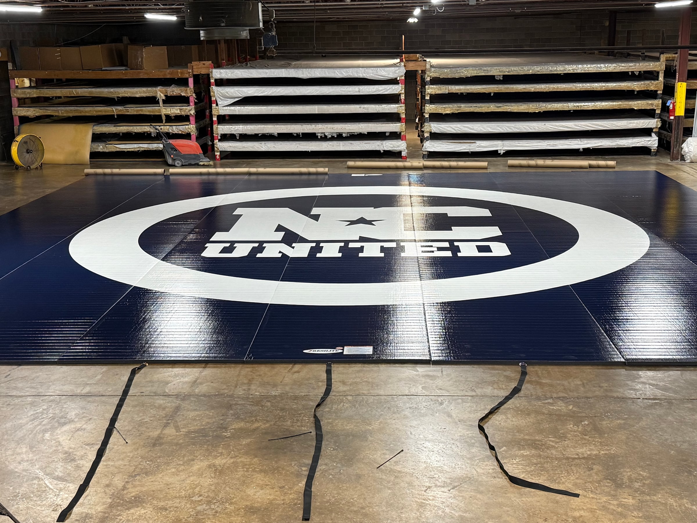 The actual navy blue Tournament of Champions Resilite wrestling mat with the white NC United logo at center